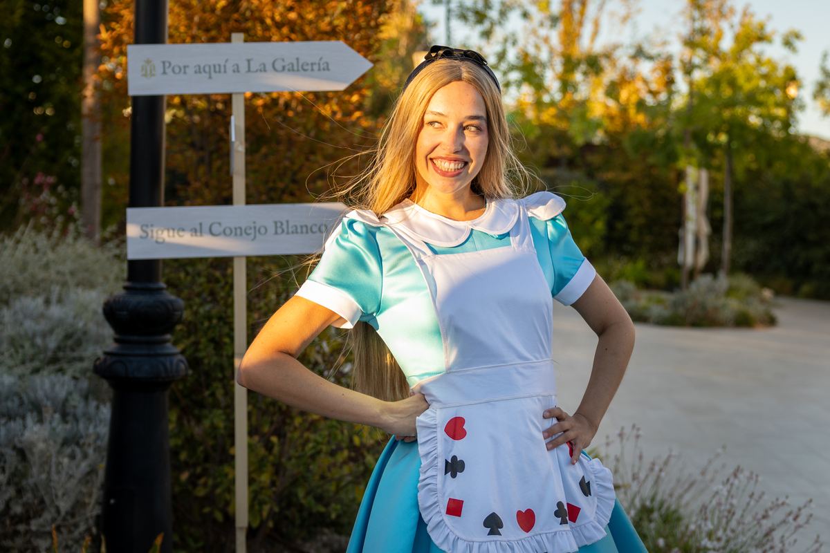 Actress dressed as Alice beside the direction signs in the garden